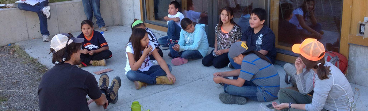 A group of students sitting on the ground outside the school, chatting and enjoying each other's company.