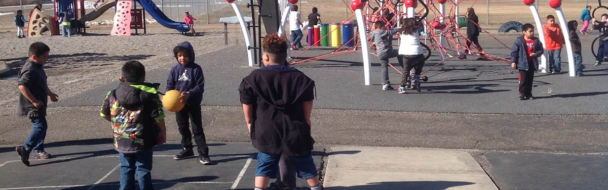 Students are playing on swings and slides at the school playground.