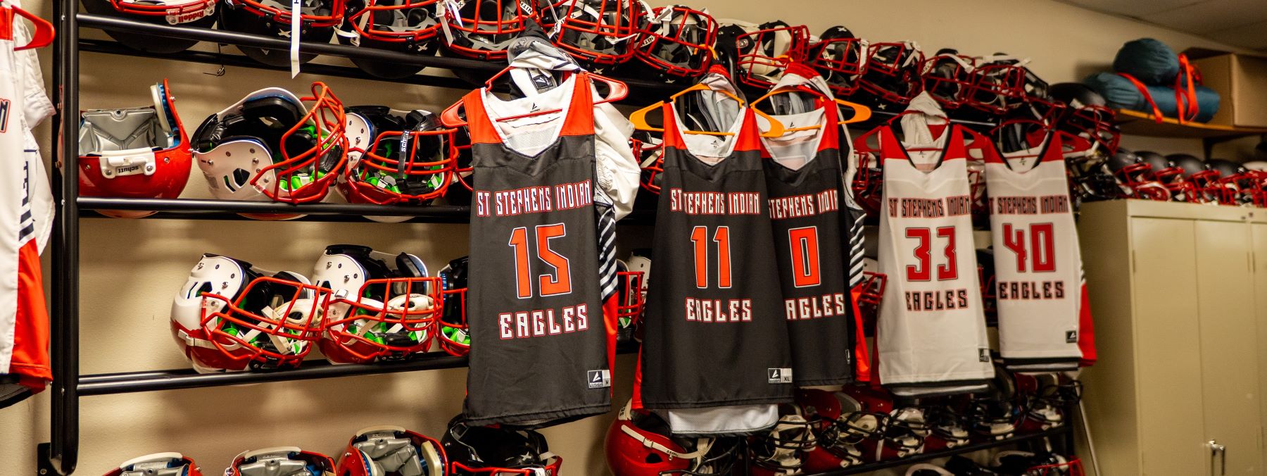 A collection of helmets and jerseys hanging on a wall, representing multiple sports teams and styles.
