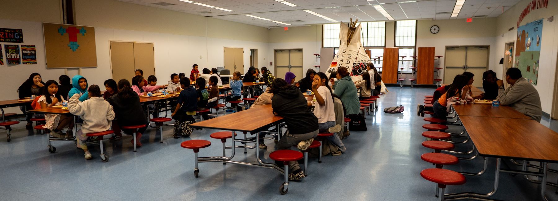 A large group of students enjoying meals together at tables in a bustling cafeteria setting.