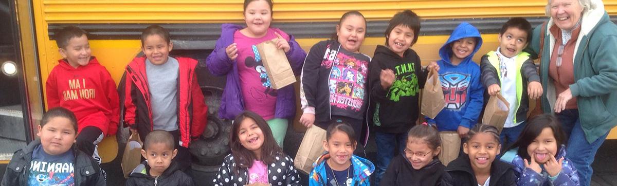A group of excited children stands in front of a yellow school bus, ready for a fun day at school.