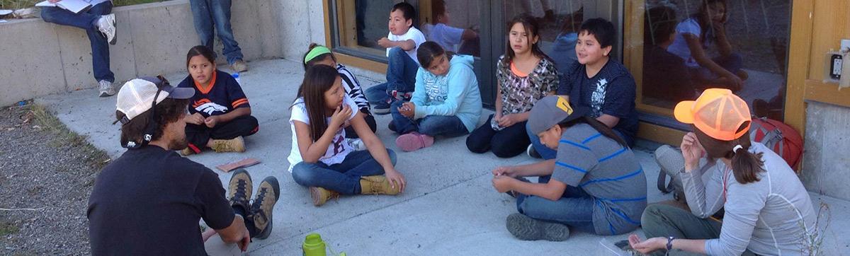 A group of students sitting on the ground outside the school, chatting and enjoying each other's company.
