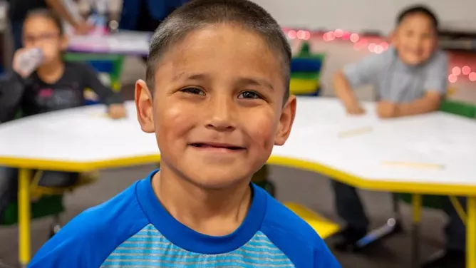 Young boy smiling at the camera in a classroom.